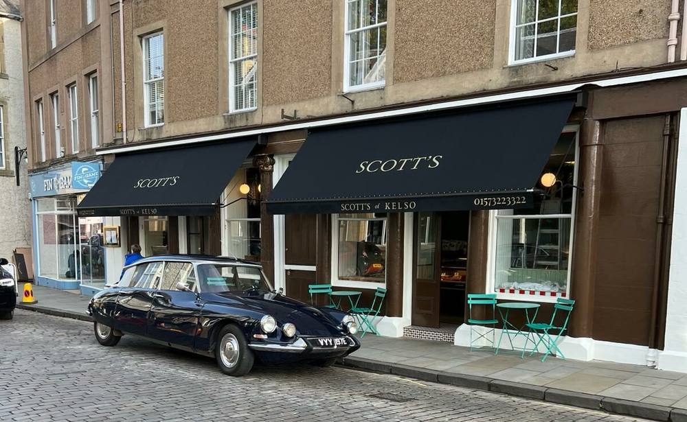 Scott's of Kelso, 44 Bridge Street, black awnings in gold lettering over a sandstone Georgian terrace, green bistro tables on the cobbles